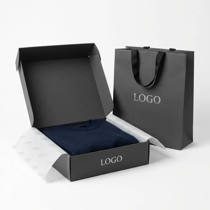 Folded navy garment in an open black custom apparel box with branded tissue paper and shopping bag