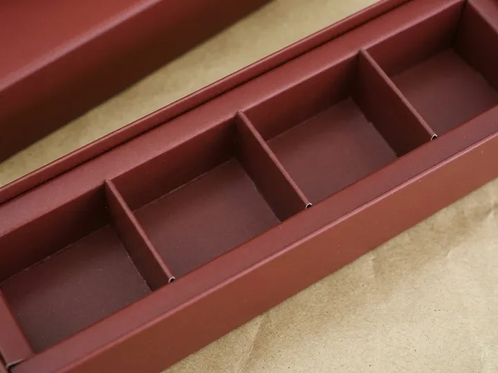 Close view of an empty folded burgundy paperboard divider with four chocolate cells