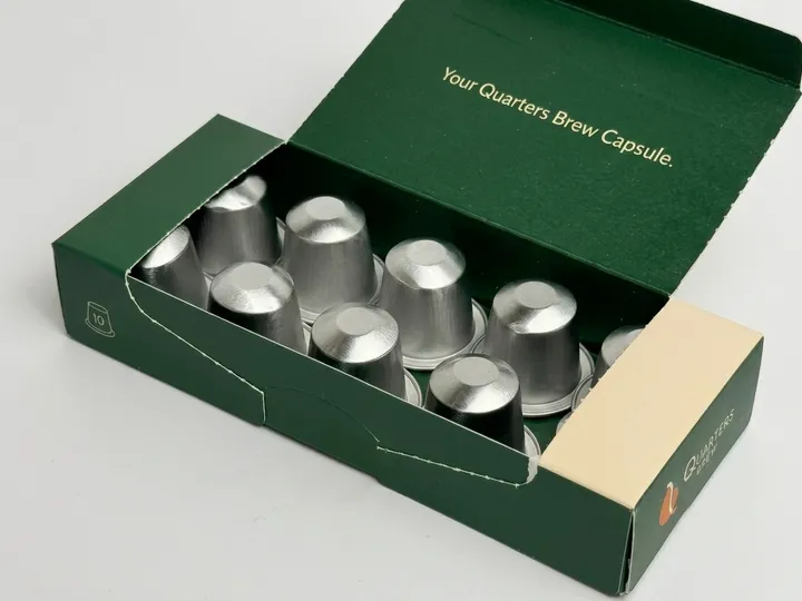 Ten silver coffee capsules arranged inside an open green custom coffee pod box
