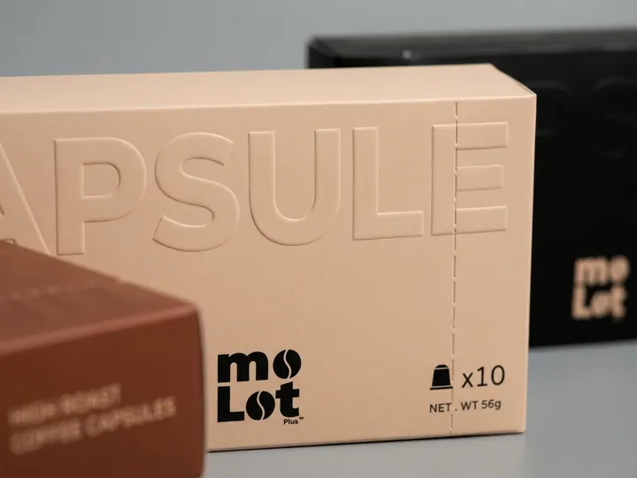 Close view of large blind embossed CAPSULE lettering on a beige coffee pod box