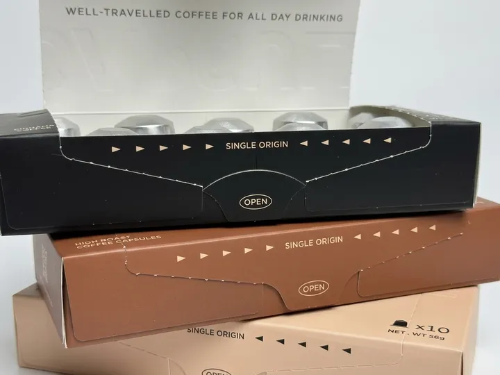 Close view of perforated tear-open front panels on black, brown, and beige coffee pod boxes