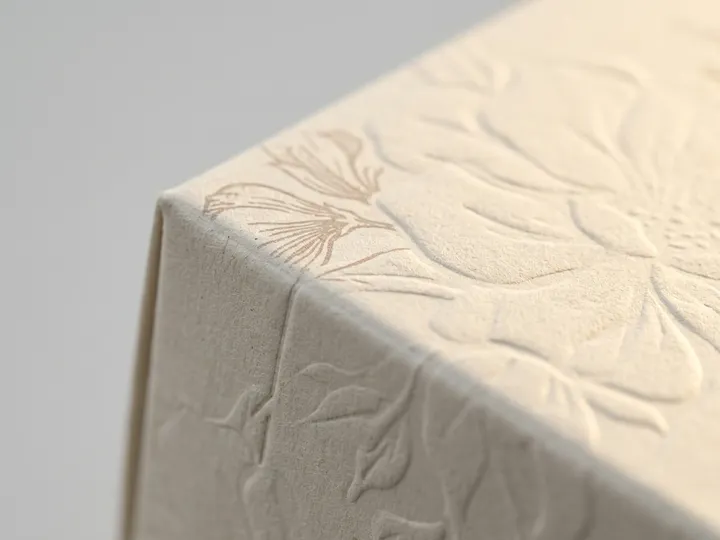 Macro view of blind floral embossing across a textured ivory paperboard fold