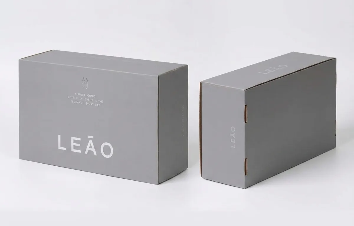 Two views of a closed gray corrugated shoe box showing the front artwork and self-locking side slots