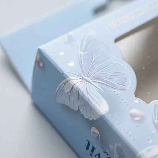 Close-up of a powder-blue eyelash carton folded edge beside the clear PET window
