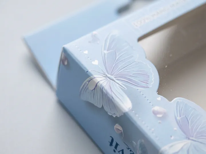 Close-up of a powder-blue eyelash carton folded edge beside the clear PET window