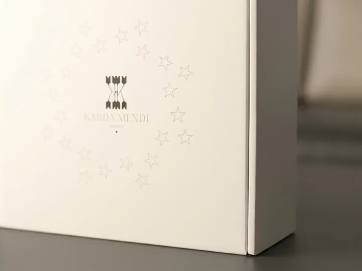 Close-up of subtle star artwork and central black logo beside a folded edge on a white hat box