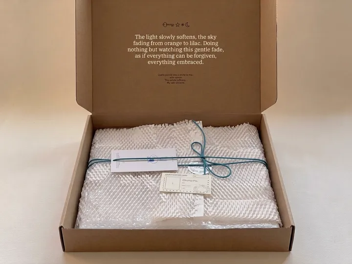 Open kraft literature mailer holding a rectangular item wrapped in honeycomb paper and tied with cotton cord