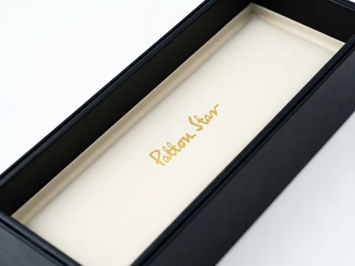 Cream lined black tie box interior with a centered gold foil script logo