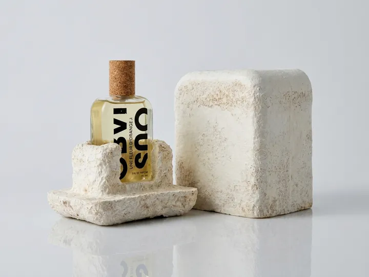 Perfume bottle seated in a custom molded mycelium base beside its cover