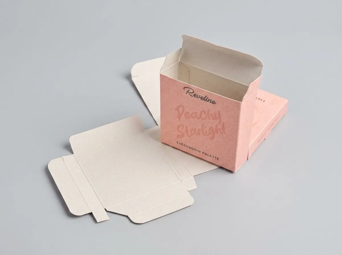 Open pink eyeshadow palette carton beside its unfolded paperboard blank