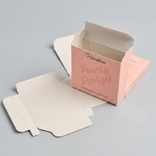 Open pink eyeshadow palette carton beside its unfolded paperboard blank