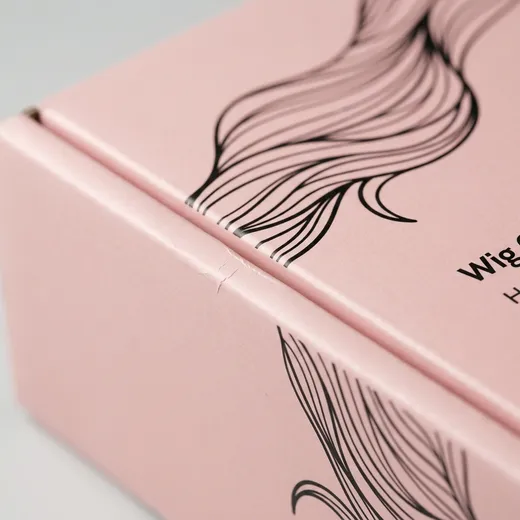 Close view of black hair artwork, pink offset print, gloss surface, score, and folded edge on a wig mailer box