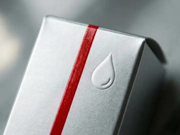 Macro close-up of glossy red UV printing on a silver matte laminated skincare serum box