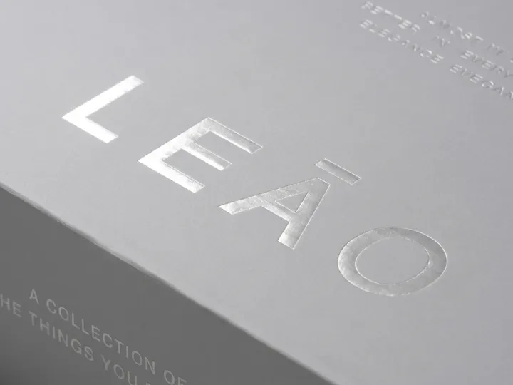 Close-up of reflective silver foil lettering on a matte gray shoe box lid beside a folded edge