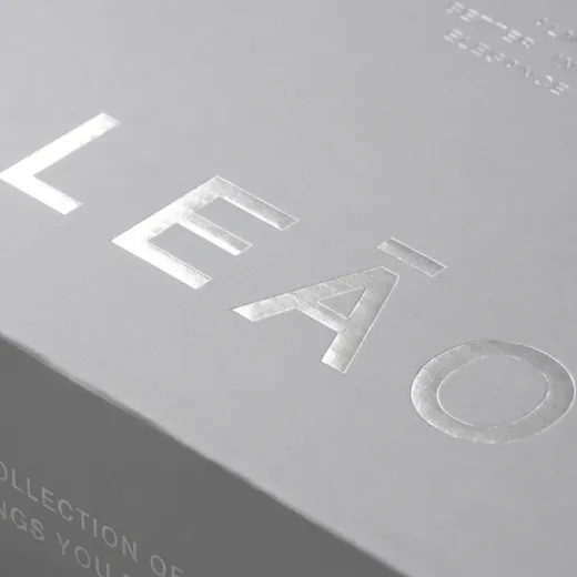 Close-up of reflective silver foil lettering on a matte gray shoe box lid beside a folded edge