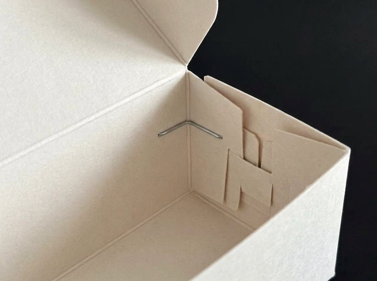 Close view inside an off-white self-locking cookie gift box showing paperboard folds and optional metal staple reinforcement